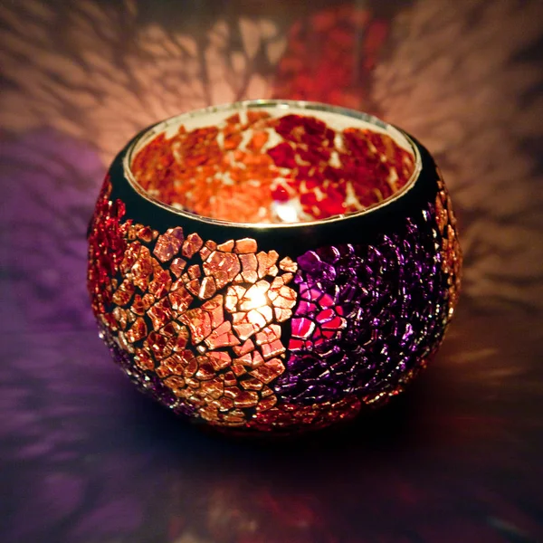 Turuncu ve mor cam içinde parlayan bir mum ışık ışınları ile bir güzel şamdan top