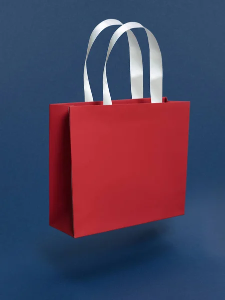 Beautiful mock-up red gift bag with white handles made of ribbons on a blue background