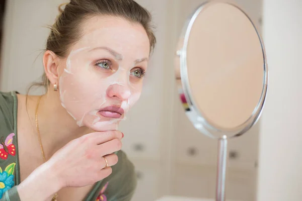 Cosmetic face mask and girl look in the mirror