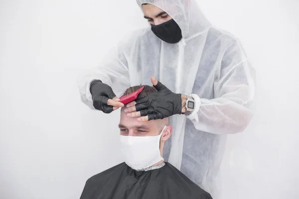 コロナウイルスの間の床屋の仕事 美容師はマスクと保護スーツ 隔離で顧客をトリミングします — ストック写真
