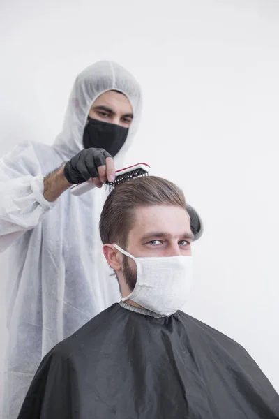 コロナウイルスの間の床屋の仕事 美容師はマスクと保護スーツ 隔離で顧客をトリミングします — ストック写真
