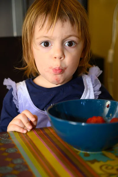 Little 3 year old girl eating strawberries at home, making different facial expressions.