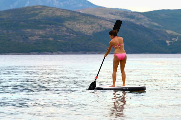Youg brunette paddling on a SUP (stand up paddle) board at the seaside of Montenegro, Adriatic sea in summer.