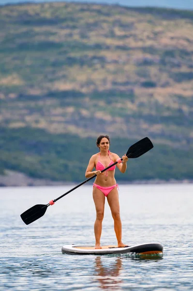 Youg brunette paddling on a SUP (stand up paddle) board at the seaside of Montenegro, Adriatic sea in summer.