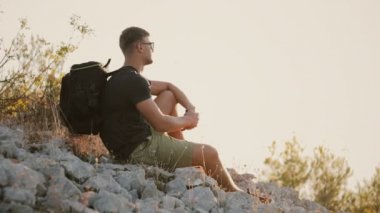 Büyük bir sırt çantası ile bir turist kayaların üzerinde oturan ve günbatımı üzerinde dinlenme