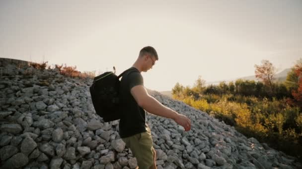 Un hombre al atardecer sube a una montaña con una mochila . — Vídeos de Stock