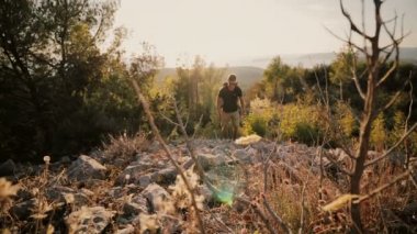 Günbatımında bir adam bir sırt çantası ile bir dağ yükselir.