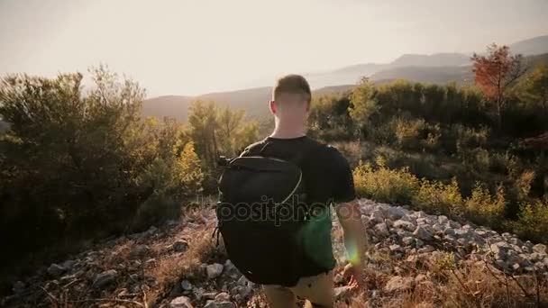Ένας άνθρωπος στο ηλιοβασίλεμα αυξάνεται σε ένα βουνό με ένα σακίδιο. — Αρχείο Βίντεο