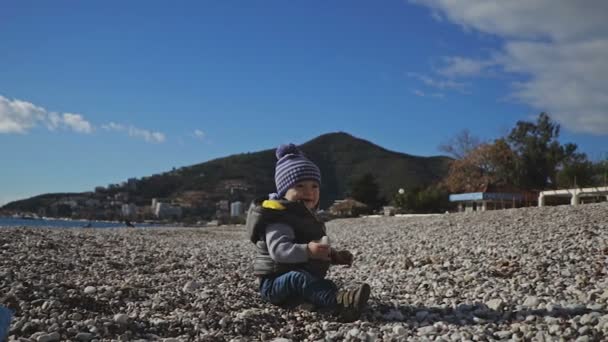 Un niño en la playa se arrastra sobre guijarros . — Vídeo de stock