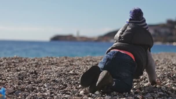 Un niño en la playa se arrastra sobre guijarros . — Vídeos de Stock