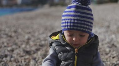 Küçük bir çocuk kameraya gülümsüyor ve oyuncaklar ile plaj üzerinde çalış.