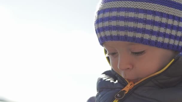 Un beau petit enfant dans un chapeau d'hiver, jouant sur la plage avec des jouets . — Video