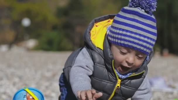 Un niño pequeño sonríe a la cámara y juega en la playa con juguetes . — Vídeo de stock