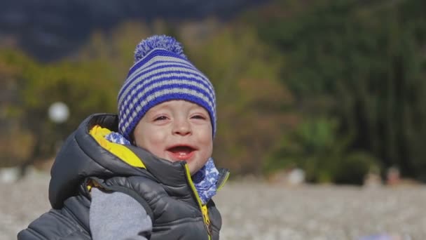 Un niño pequeño sonríe a la cámara y juega en la playa con juguetes . — Vídeo de stock