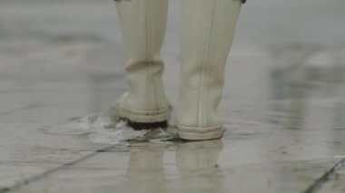 Yağmurlu hava durumu için iyi bir ruh hali. Beyaz lastik çizmeli, yüksek korsan botlu, su birikintisinde su sıçratan bir kadın.