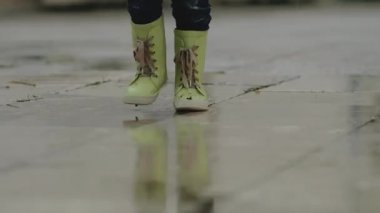 Lastik çizmeli küçük çocuk yağmur sırasında su birikintisinde duruyor.