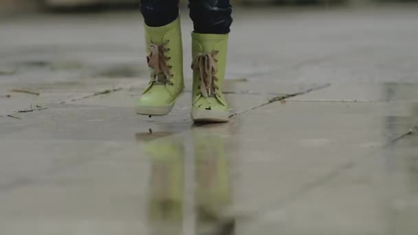 Маленький мальчик в резиновых сапогах стоит в луже во время дождя — стоковое видео