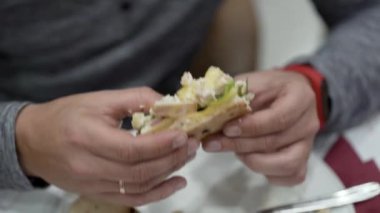 Adam tavuklu mayonezli sandviç yiyor.