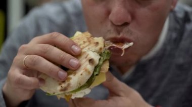 Adam tavuklu mayonezli sandviç yiyor.