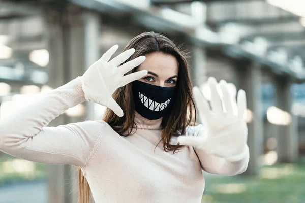 Ung flicka i rolig medicinsk mask och handskar visar stopp tecken Stockbild