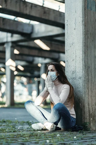 Koruyucu maskeli ve steril eldivenli bir kız otoparkta oturuyor.