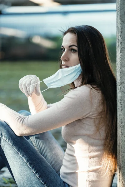 Una joven con guantes de goma se sienta y sostiene una mascarilla protectora — Foto de Stock