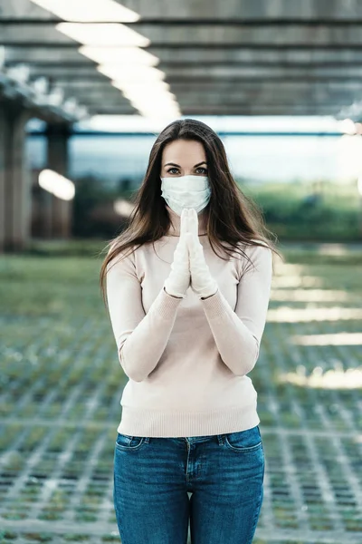 Yüzünde koruyucu maske takmış güzel bir kız ve lastik eldivenler dua ediyor.