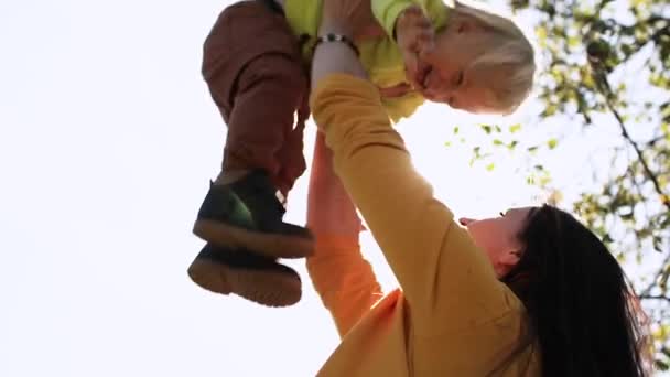 Giovane madre getta bambino con le mani i raggi del sole brillano nella fotocamera — Video Stock