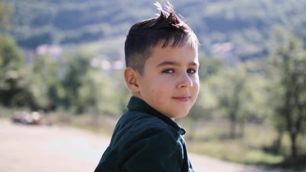 8-летний мальчик смотрит в камеру на фоне красивых гор — стоковое видео