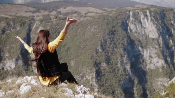 La chica se sienta en la cima de la montaña extiende sus manos soplando viento — Vídeos de Stock