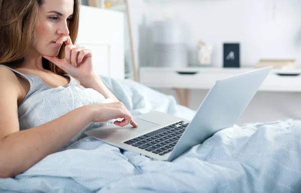 Chica joven con ordenador portátil comprobar las redes sociales en la cama en casa —  Fotos de Stock