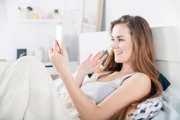 Mladá dívka ležela v posteli a video volání na telefonu — Stock fotografie