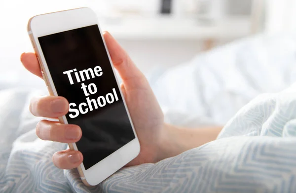 Time to School on smart phone screen, girl lying in bed — Stock Photo, Image