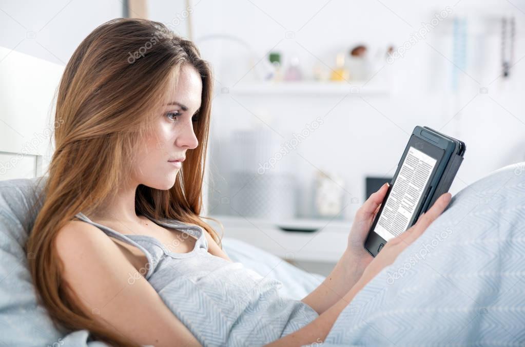 Girl reading ebook on tablet reader in bed at home