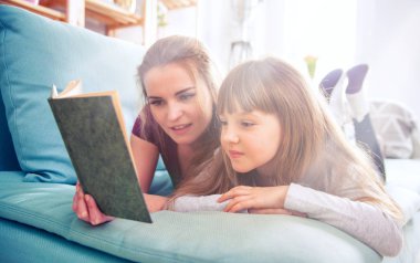 Anne ve kızı koltukta oturan ve birlikte kitap okuma