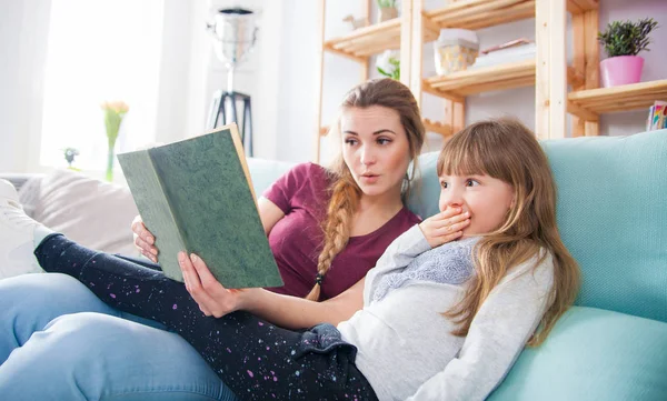 Anya és lánya kanapén ül, és könyvet olvas együtt — Stock Fotó