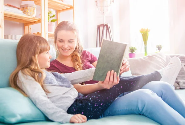 Mãe e filha sentados no sofá e lendo livro juntos — Fotografia de Stock