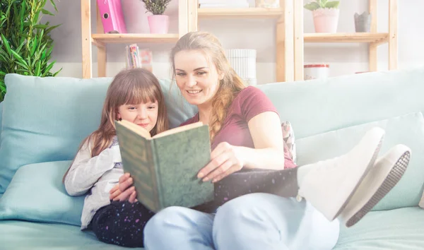 Anya és lánya kanapén ül, és könyvet olvas együtt — Stock Fotó