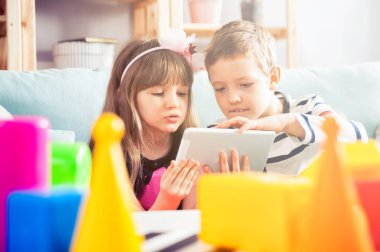 Evde kanepede oturan ve pc tablet ile birlikte oynayan kardeşler