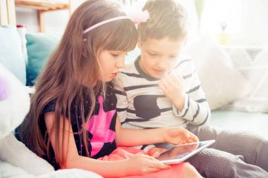 Evde kanepede oturan ve pc tablet ile birlikte oynayan kardeşler