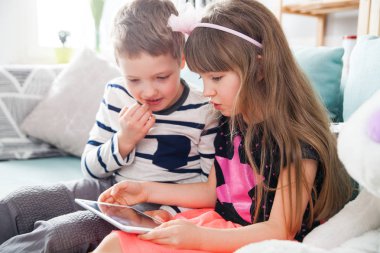 Evde kanepede oturan ve pc tablet ile birlikte oynayan kardeşler