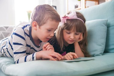 Evde koltukta yalan ve tablet ile birlikte oynayan mutlu kardeşler
