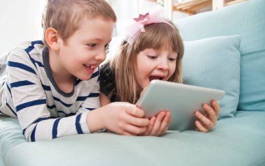Evde koltukta yalan ve tablet ile birlikte oynayan mutlu kardeşler