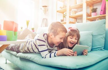 Evde koltukta yalan ve tablet ile birlikte oynayan mutlu kardeşler