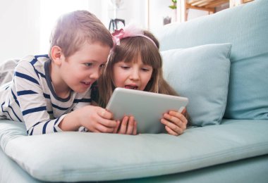 Evde koltukta yalan ve tablet ile birlikte oynayan mutlu kardeşler