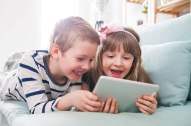 Evde koltukta yalan ve tablet ile birlikte oynayan mutlu kardeşler