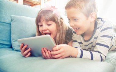 Evde koltukta yalan ve tablet ile birlikte oynayan mutlu kardeşler