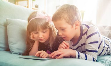 Evde koltukta yalan ve tablet ile birlikte oynayan mutlu kardeşler