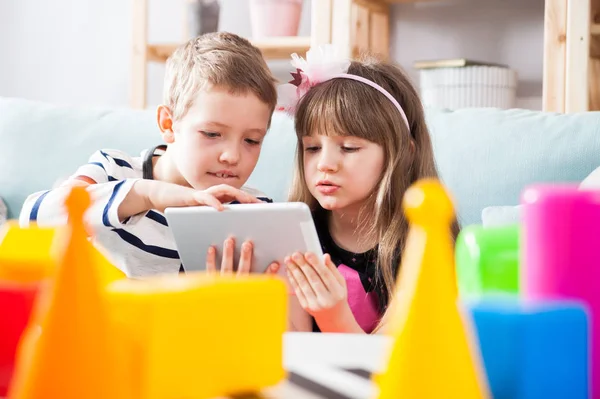 Siblings sitting on sofa at home and playing with pc tablet together — Stock Photo, Image