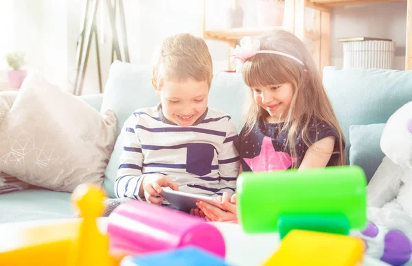 Irmãos sentados no sofá em casa e brincando com tablet pc juntos — Fotografia de Stock